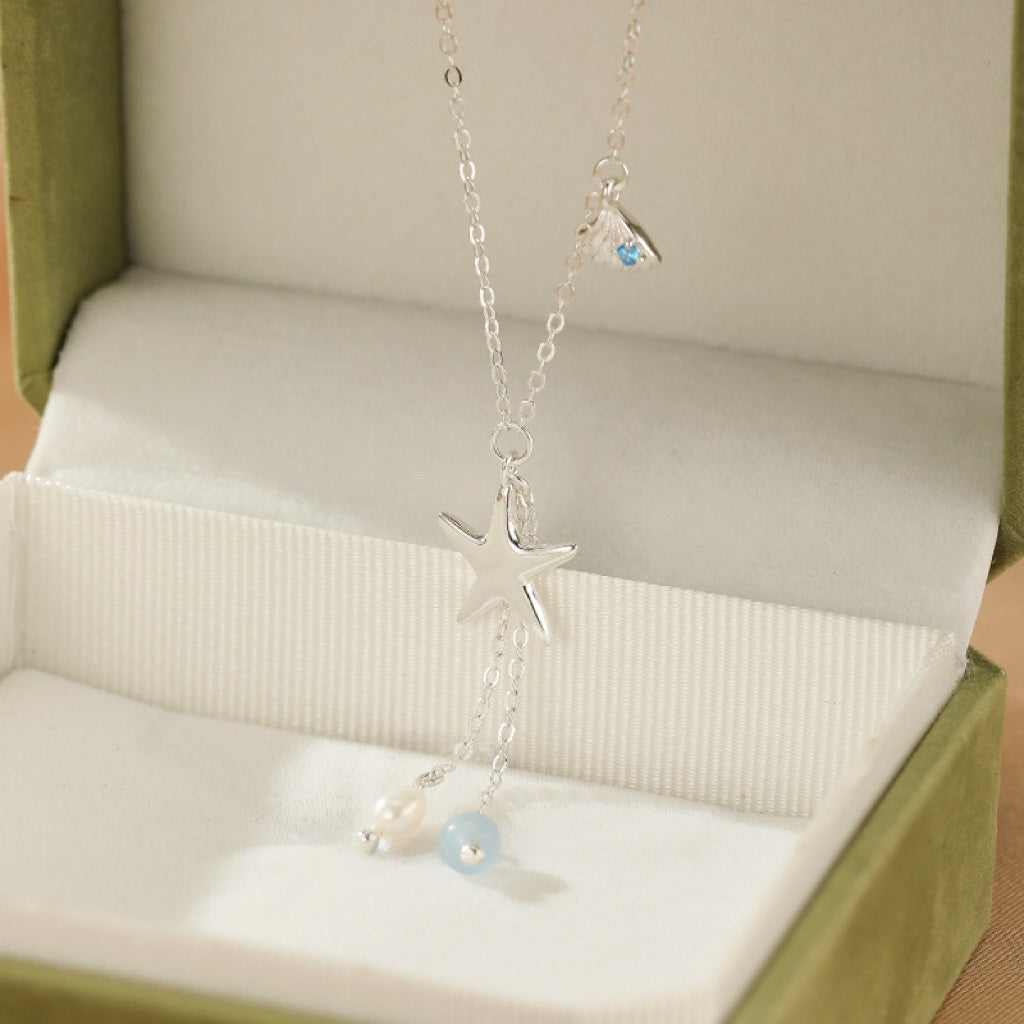 Collier "Étoile des Mers" en argent S925, orné d'une étoile, d'une perle et d'une pierre bleu aigue-marine, présenté dans une écrin vert.