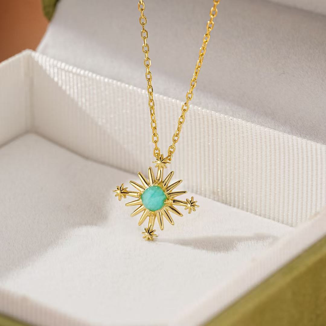 Collier en argent plaqué or avec pendentif en forme de croix étoilée sertie d'une pierre d'amazonite turquoise, présenté dans une boîte cadeau verte.