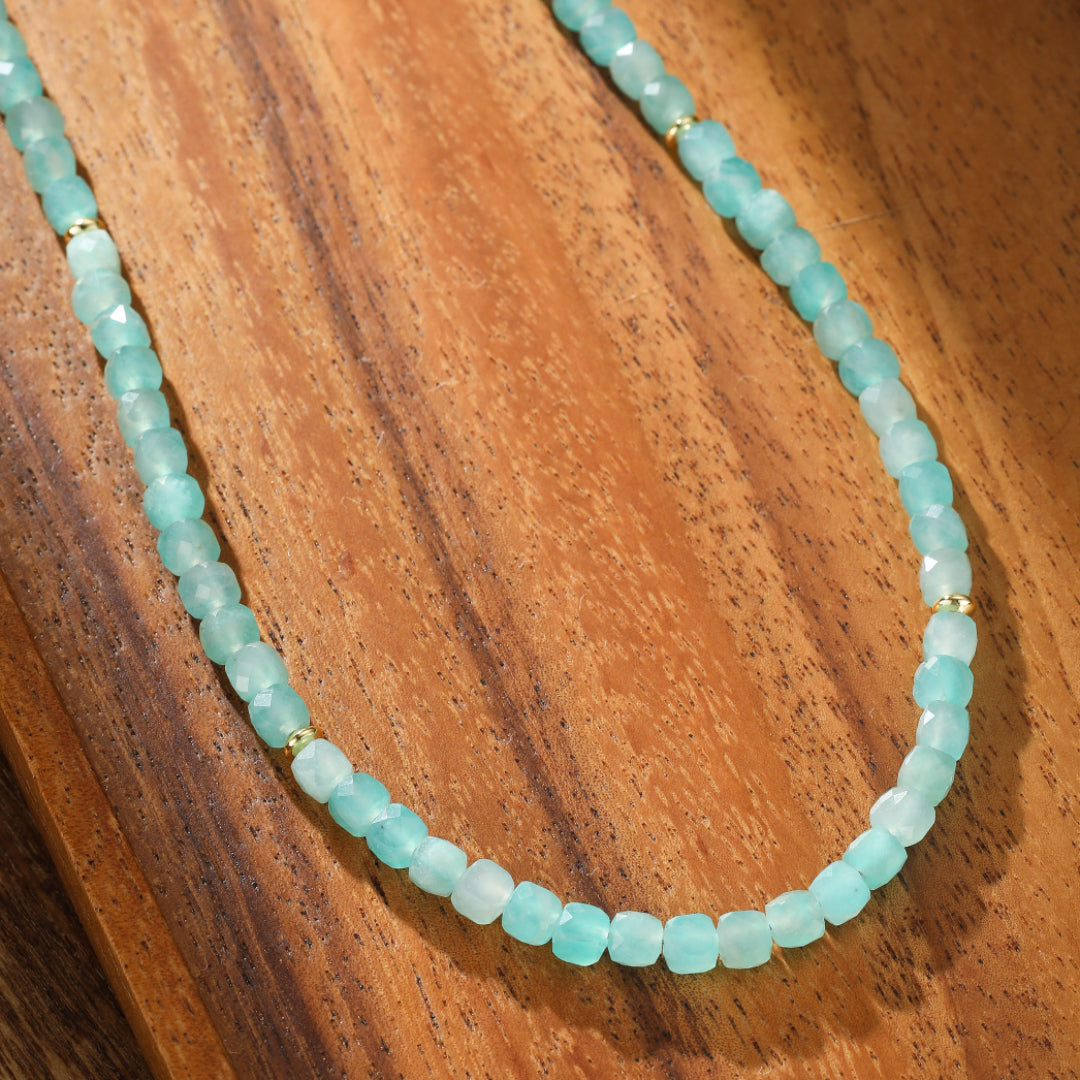 Collier en amazonite aux teintes bleutées et dorées, orné de petites perles facettées et de quelques perles dorées, posé sur un fond en bois.
