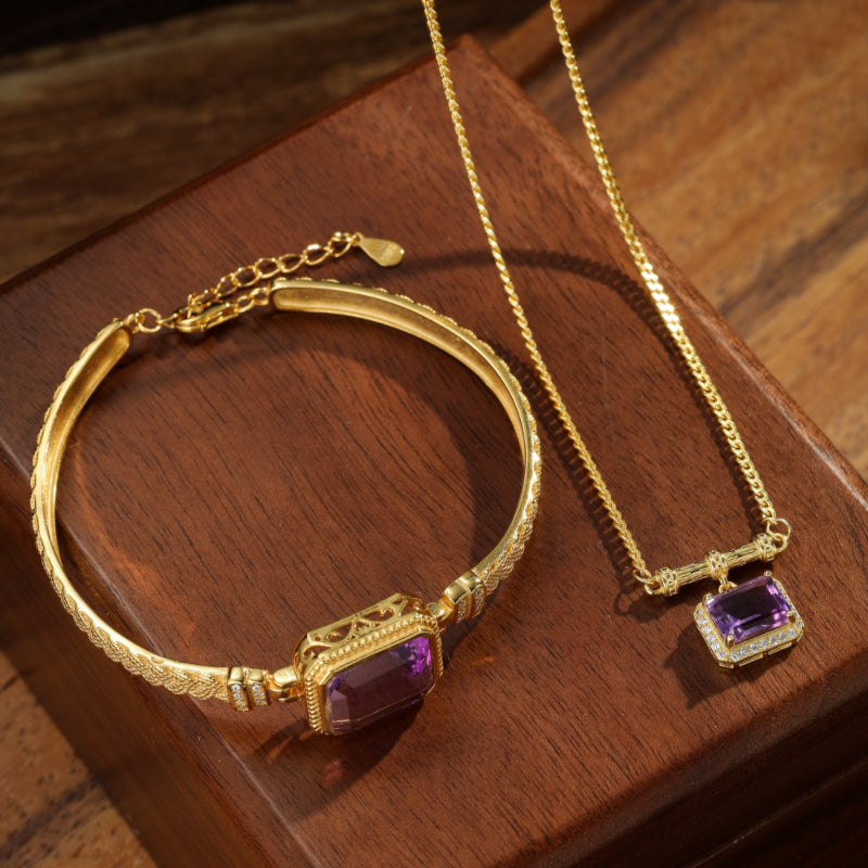 Ensemble de bijoux en argent plaqué or avec un bracelet et un collier ornés de pierres d'améthyste violettes rectangulaires sur un fond en bois.