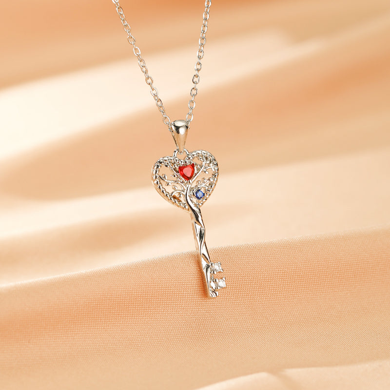 Collier Arbre de Vie en argent avec un pendentif en forme de clé et de cœur orné de pierres rouges et bleues.