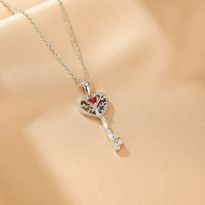 Collier en argent en forme de clé avec un cœur orné d'un arbre de vie, de pierres rouges et bleues et de cristaux brillants.