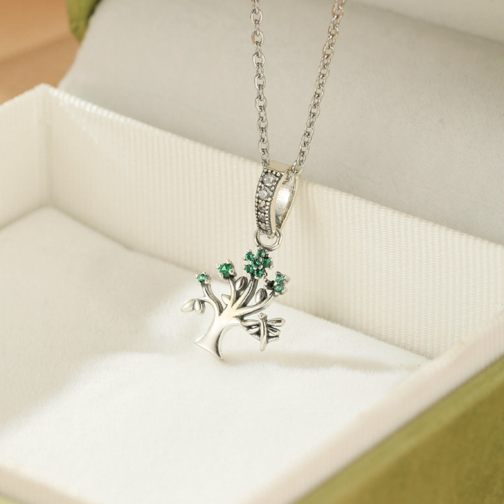Collier Arbre de Vie en argent avec des petites pierres vertes, montrant des branches détaillées et un fermoir orné de cristaux.