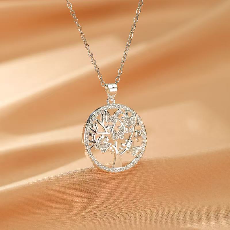 Collier Arbre de Vie en argent avec des papillons et des pierres scintillantes, sur fond satiné couleur pêche.