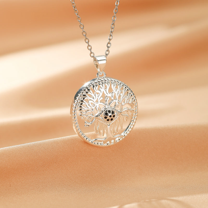 Collier Arbre de Vie en argent avec un pendentif rond ajouré représentant un arbre aux racines profondes et un centre orné de petites pierres noires.