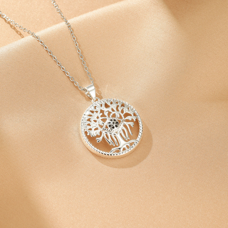 Collier Arbre de Vie argenté avec un pendentif rond orné d'un arbre stylisé aux branches détaillées et d'une petite pierre noire au centre, suspendu à une fine chaîne.