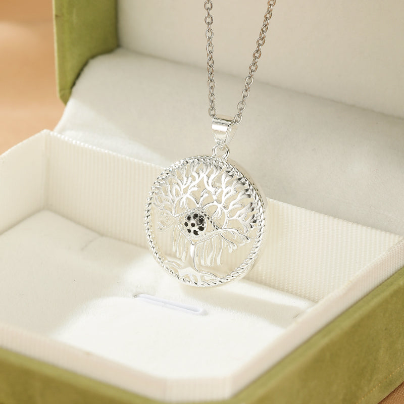 Collier Arbre de Vie en argent avec un pendentif rond ouvragé représentant un arbre stylisé avec un centre noir, présenté dans une boîte verte.