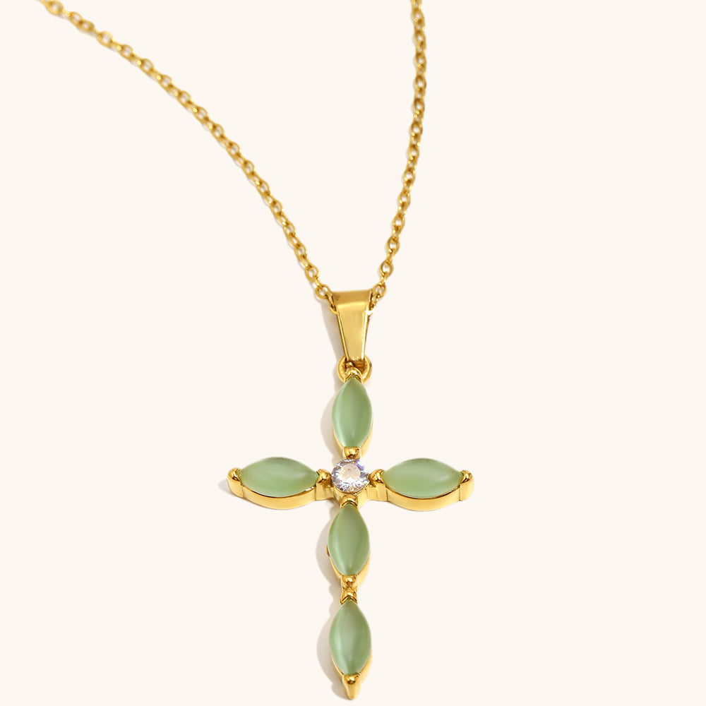 Collier en or avec un pendentif en forme de croix orné de pierres vertes en forme de feuilles et d'une petite pierre transparente au centre, sur fond blanc.