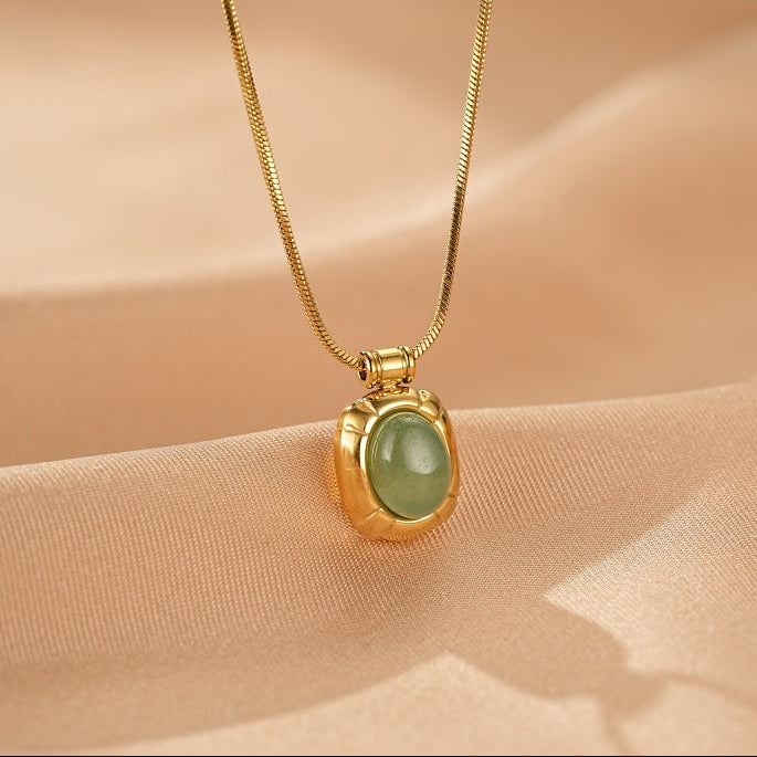 Collier plaqué or avec un pendentif carré orné d'une pierre d'aventurine verte ovale, sur fond texturé beige.