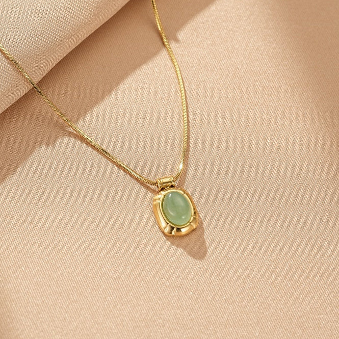 Collier en or avec un pendentif ovale en aventurine verte, sur un fond texturé de couleur crème.