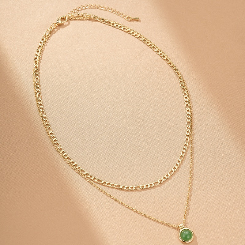 Collier double chaîne dorée avec un pendentif rond en aventurine verte au centre.