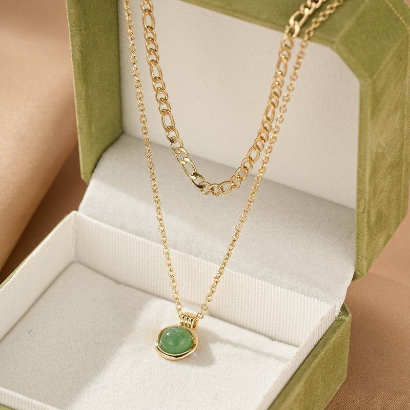 Collier Aventurine – Trésor du Cœur, un collier double chaîne doré avec un pendentif rond en aventurine verte, présenté dans une boîte cadeau verte.