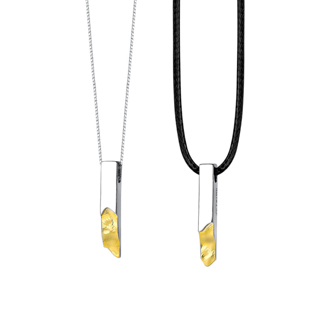 Deux pendentifs argentés sur des chaînes, l'un en argent avec une incrustation dorée brute, l'autre sur un cordon noir avec une incrustation dorée brute, symbolisant un lien de couple.