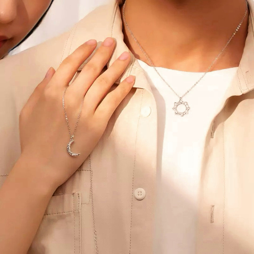 Ensemble de deux colliers en argent, l'un avec un pendentif lune, l'autre avec un pendentif soleil, portés par un couple.