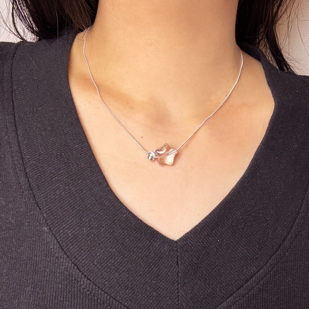 Collier en argent avec un pendentif en forme d'étoile en cristal de roche transparent et une petite bille argentée.