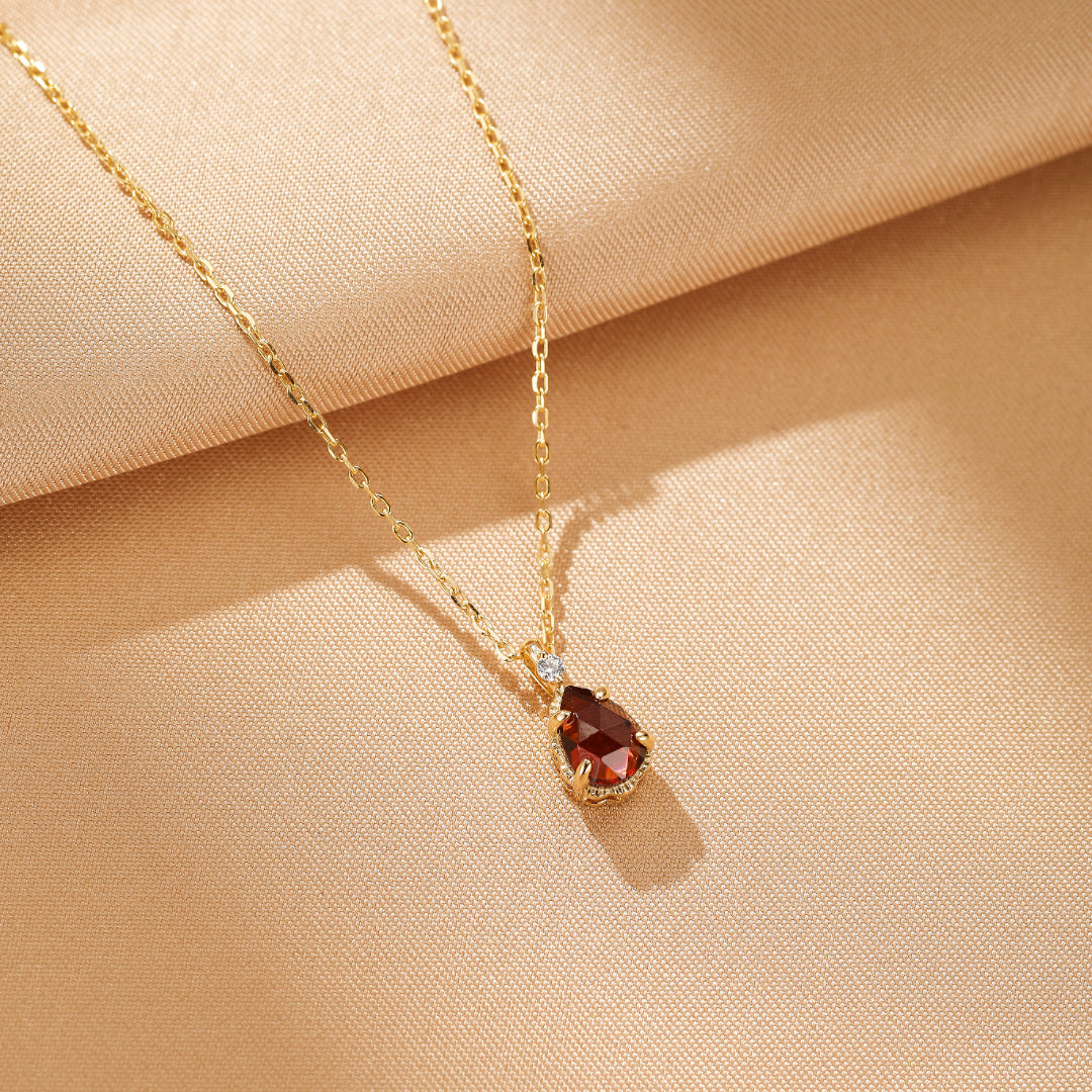Collier fin en argent plaqué or avec un pendentif en forme de goutte d'eau en grenat rouge profond et une petite pierre d'accent blanche.