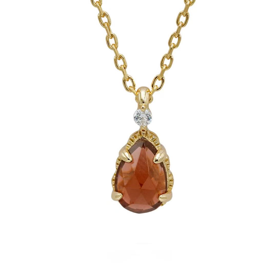 Collier en argent plaqué or avec un pendentif en forme de goutte de grenat carmin faceté, serti sur un petit diamant, le bijou est suspendu à une chaîne.