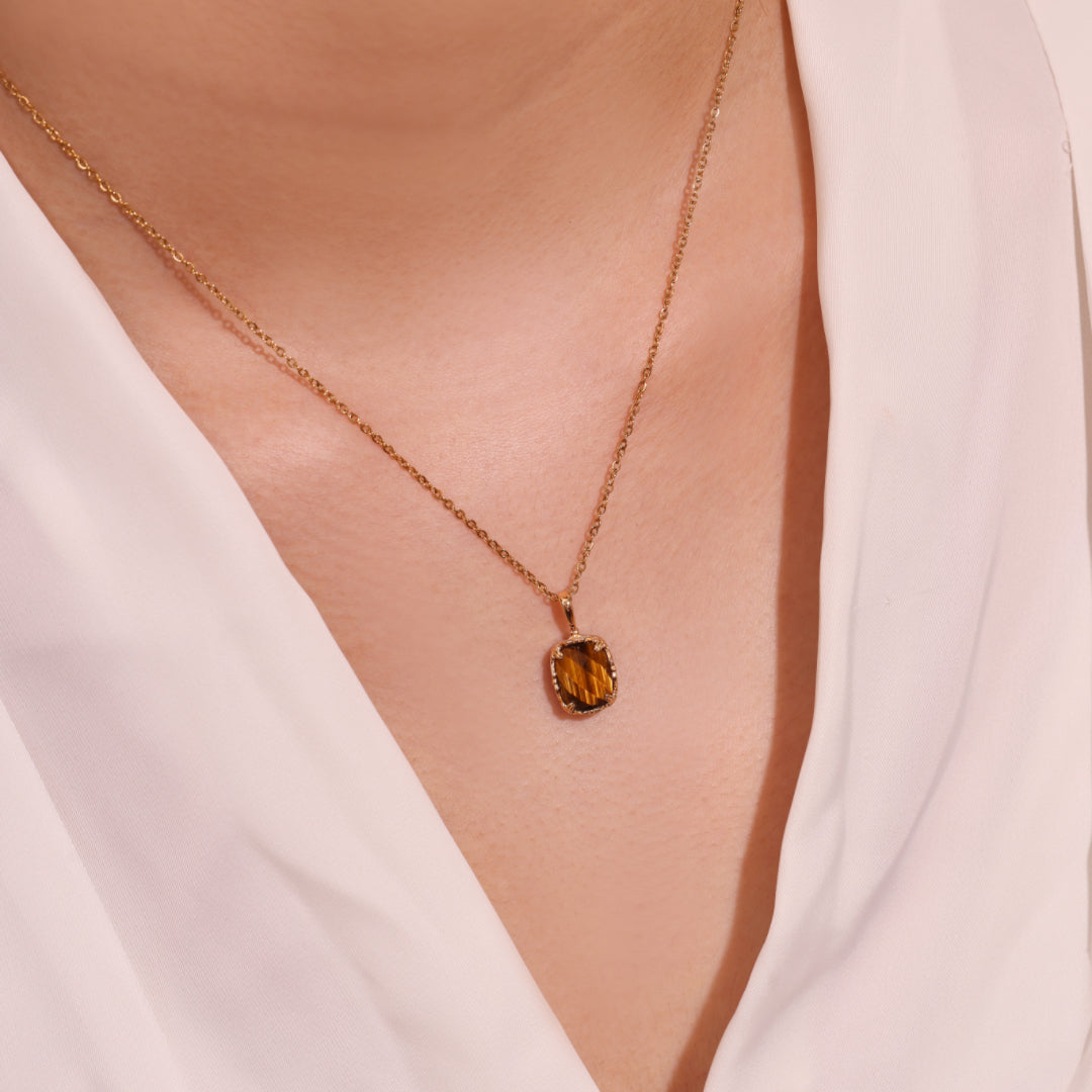 Collier en plaqué or avec pendentif œil de tigre carré, porté par une femme vêtue de blanc.