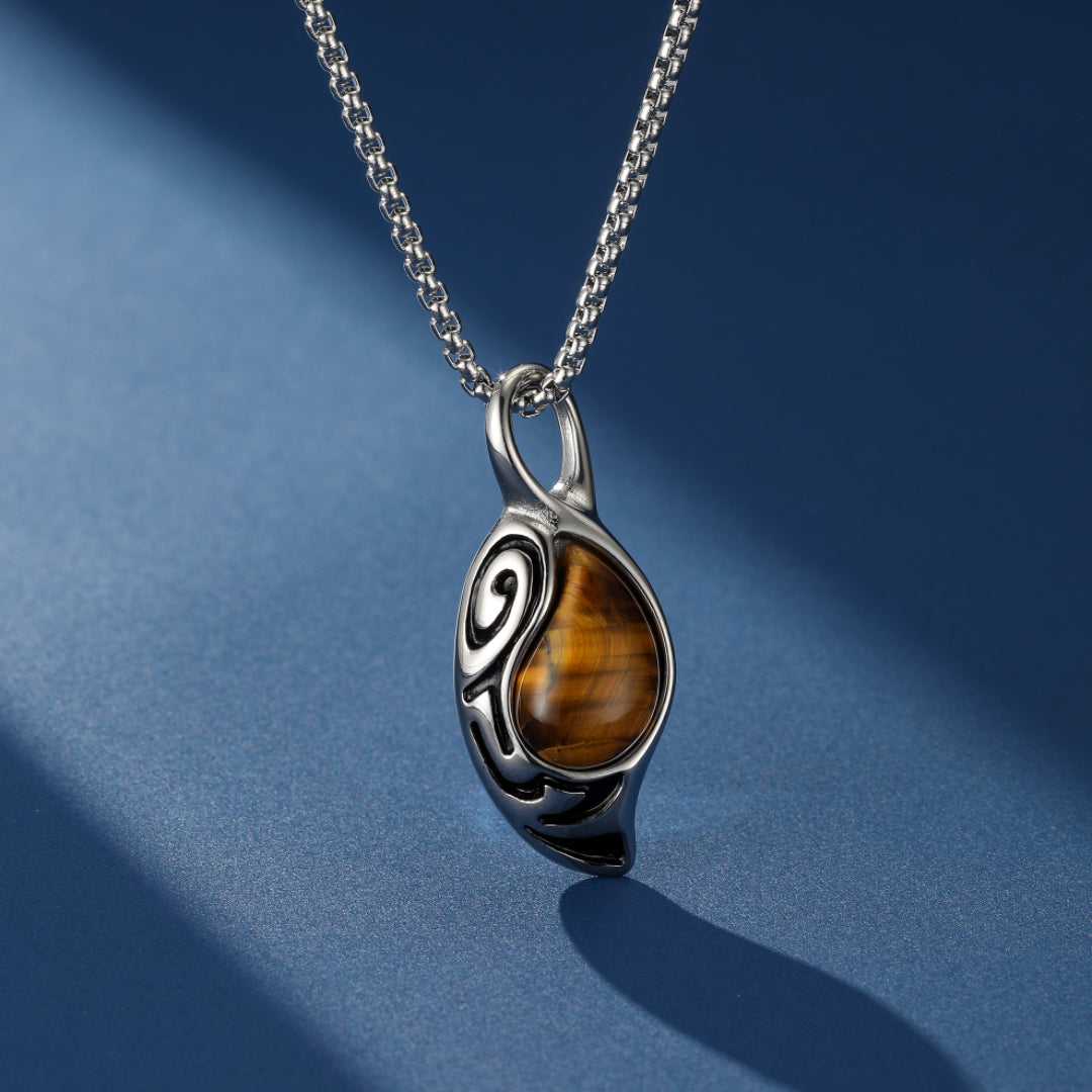 Collier argenté avec pendentif en œil de tigre aux motifs stylisés représentant un tourbillon et une flamme, sur fond bleu avec ombre.