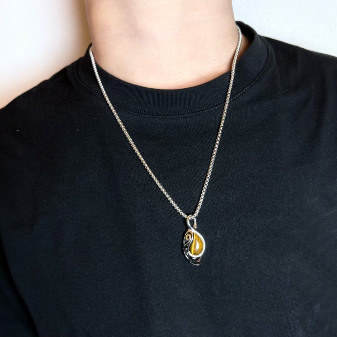 Collier avec pendentif en œil de tigre sur fond noir, porté par un homme.
