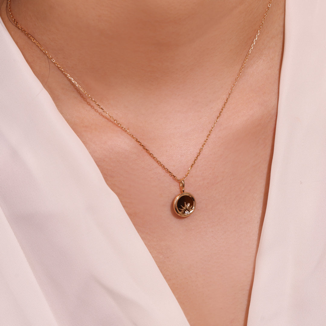 Collier en argent plaqué or avec un pendentif rond serti d'une pierre œil de tigre et d'un zircon scintillant, porté autour du cou par une femme.