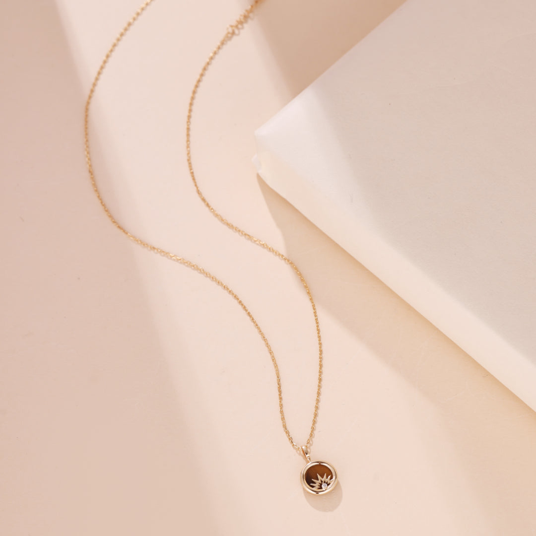 Collier pendentif rond avec œil de tigre marron et motif soleil stylisé, sur une fine chaîne en argent plaqué or.