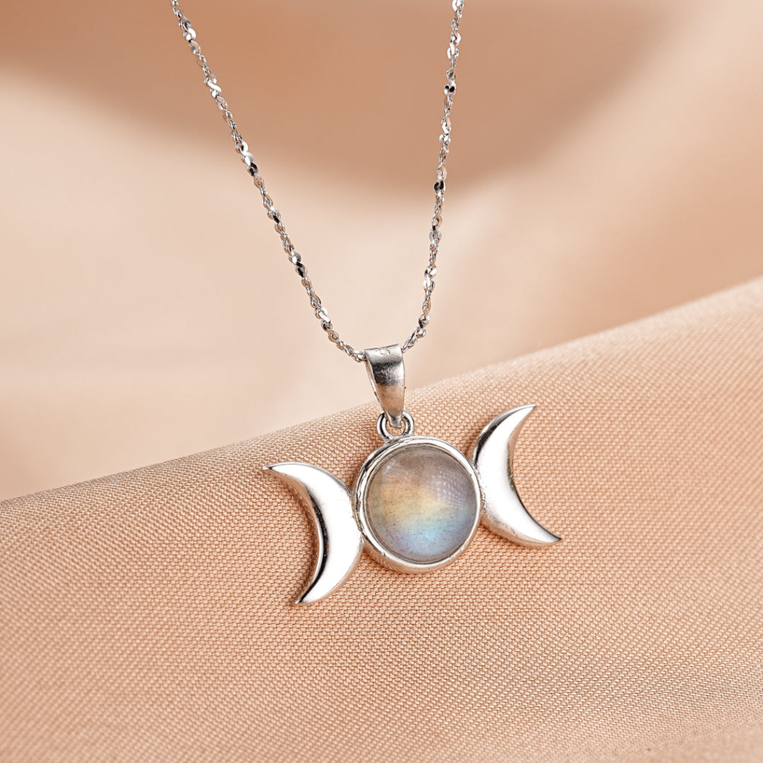Collier triple lune en argent avec une pierre de labradorite irisée au centre, sur un fond de tissu beige satiné.