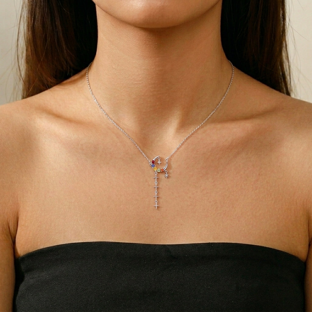Collier en argent avec un pendentif en forme de croissant de lune orné de pierres colorées et de petites étoiles tombantes.