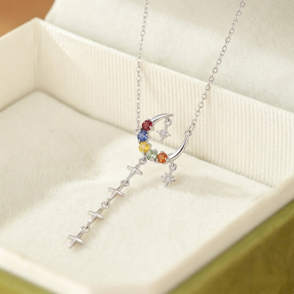 Collier en argent avec un croissant de lune orné de pierres naturelles multicolores et une chaîne tombante de petites croix. Un pendentif étoile scintille à côté de la lune.