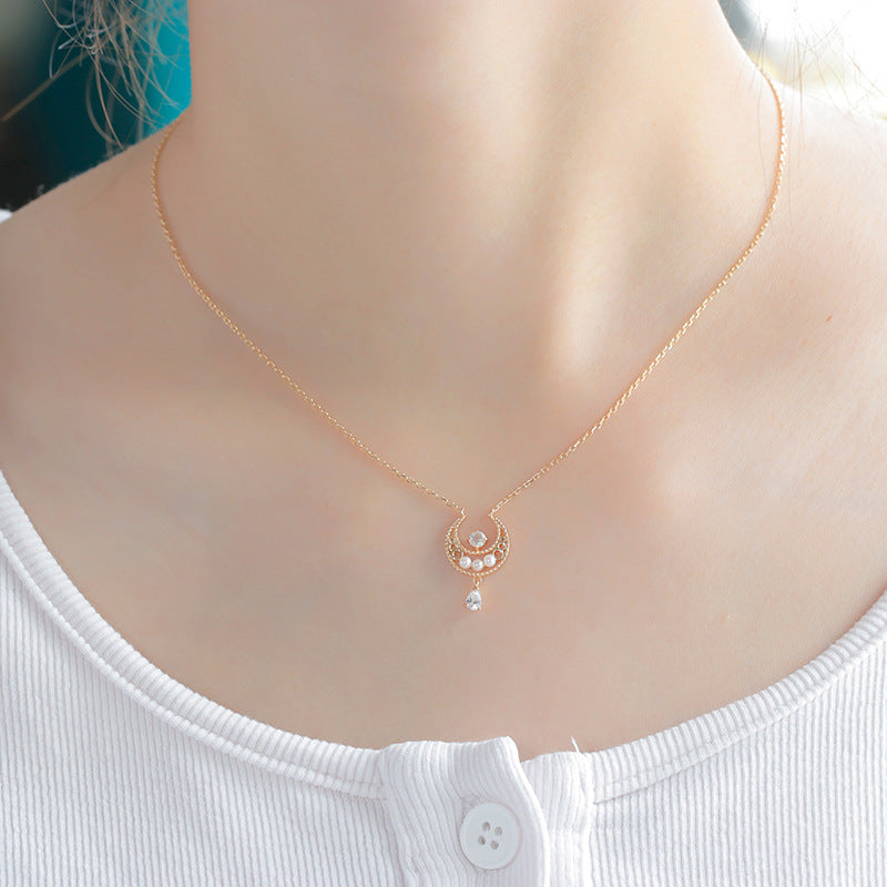 Un collier en argent plaqué or avec un pendentif en forme de croissant de lune orné de petites perles et d'une gouttelette de pierre de lune, porté par une femme.