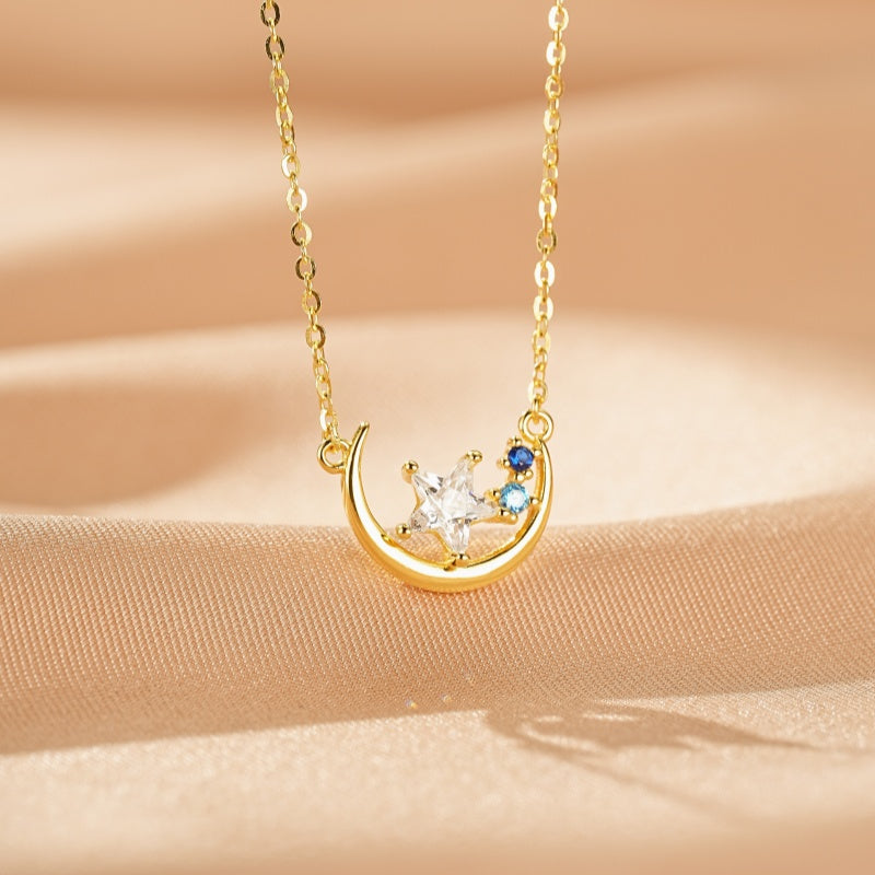 Collier en argent plaqué or 16K avec un croissant de lune orné d'une étoile blanche et de deux petites pierres bleues.