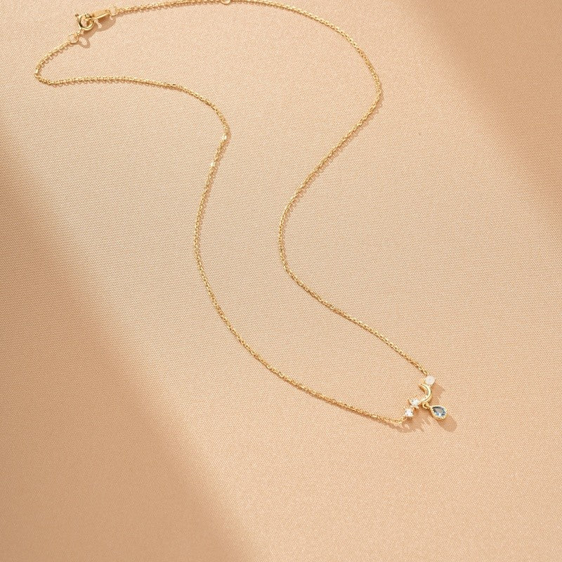 Collier fin en argent plaqué or 14 carats avec un pendentif en forme de croissant de lune orné d'une topaze bleue et de petites pierres scintillantes.