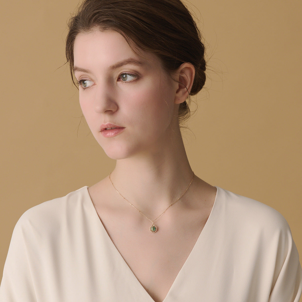 Un collier en argent plaqué or avec un pendentif rond en malachite et quartz rutile, porté par une femme.