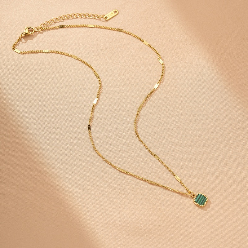 Collier plaqué or avec un pendentif carré en malachite verte striée, sur un fond rose poudré.