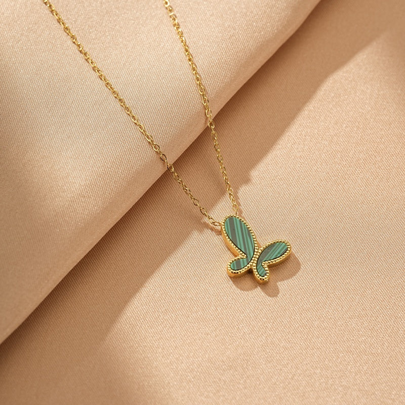 Collier en or avec un pendentif en forme de papillon en malachite verte rayée, sur fond beige