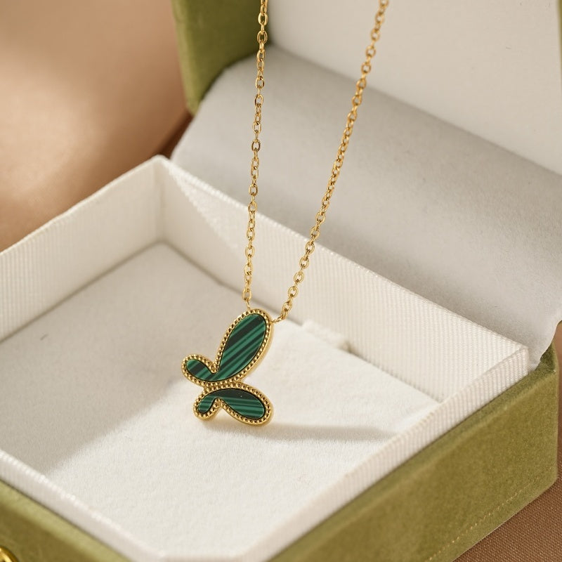 Collier plaqué or avec un pendentif en forme de papillon orné de malachite verte aux rayures caractéristiques, posé dans un écrin ouvert.