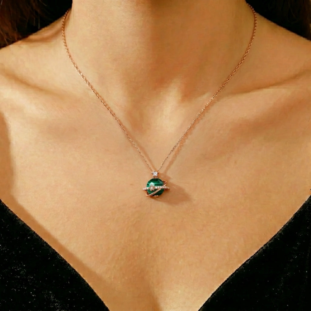 Collier avec un pendentif en forme de planète orné d'une sphère de malachite verte et d'anneaux incrustés de zircons, monté sur une chaîne plaquée or rose.