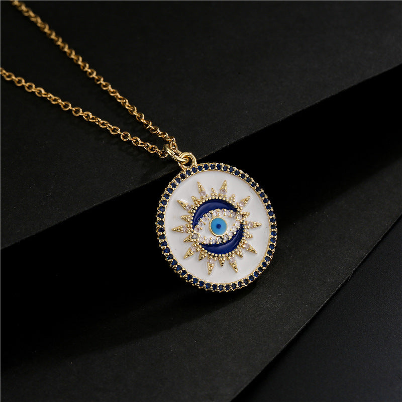 Collier tendance avec un pendentif rond orné d'un œil bleu et blanc entouré de cristaux et de petites pierres bleues, sur une chaîne dorée.