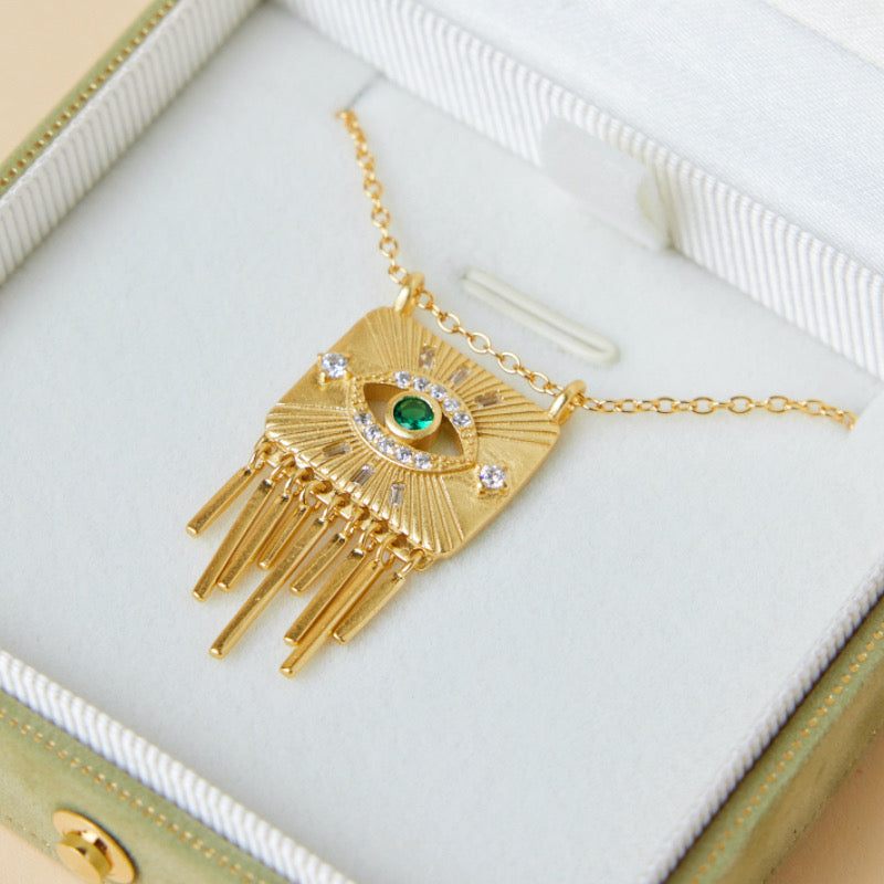 Collier tendance en argent plaqué or avec un pendentif carré orné d'un œil stylisé serti d'une émeraude et entouré de zirconiums, avec des franges tombantes.