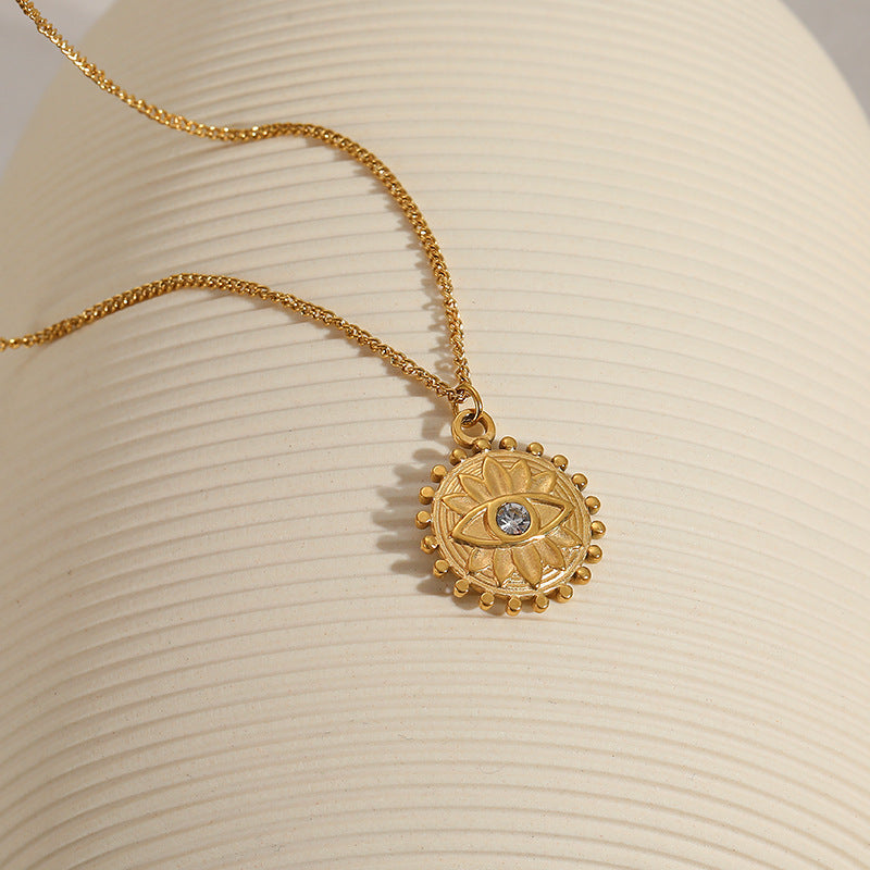 Collier en or avec un pendentif rond gravé d'un œil stylisé et de motifs solaires, orné d'une petite pierre bleue au centre.