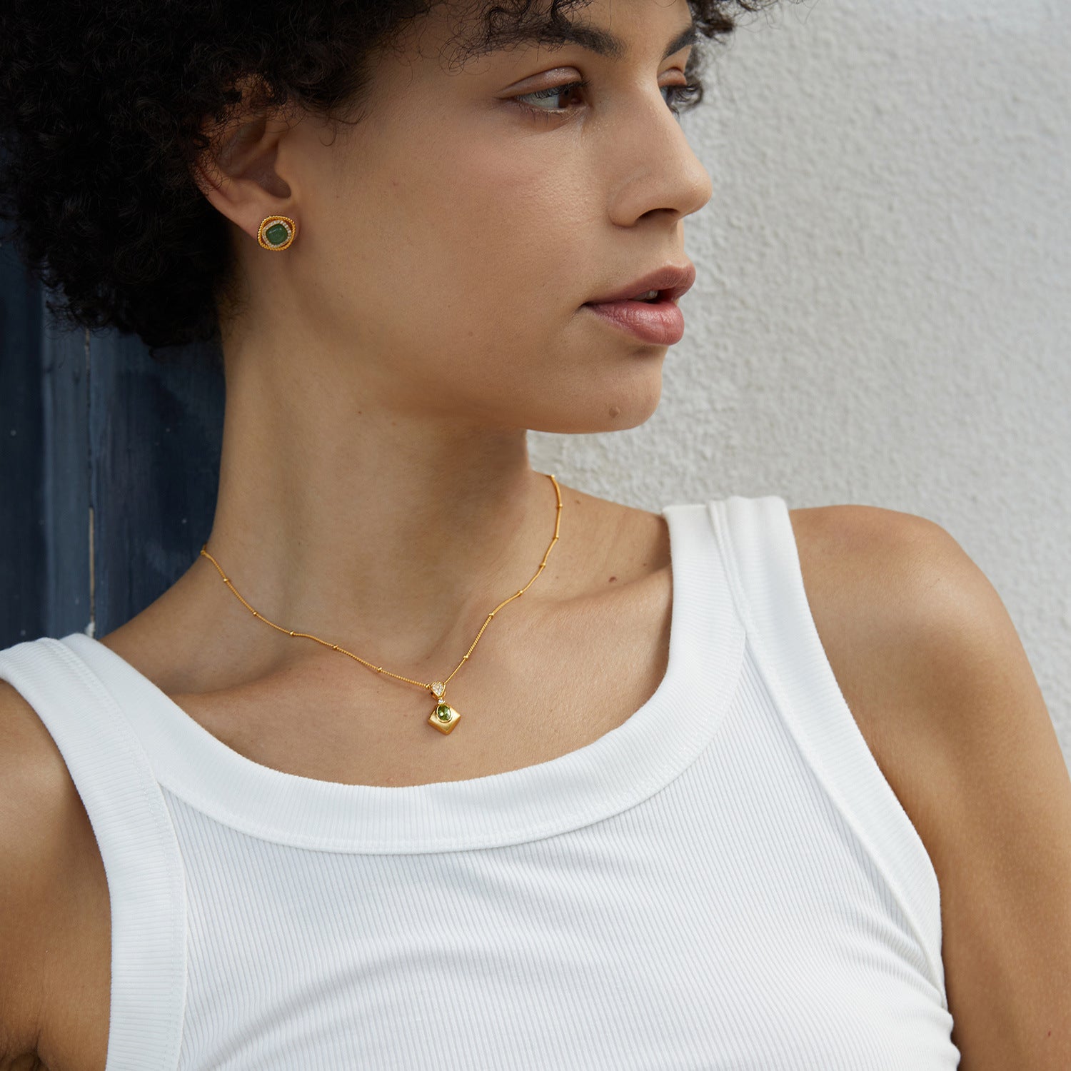 Collier plaqué or avec pendentif carré vert et petites perles, porté par une femme avec des boucles d'oreilles assorties.