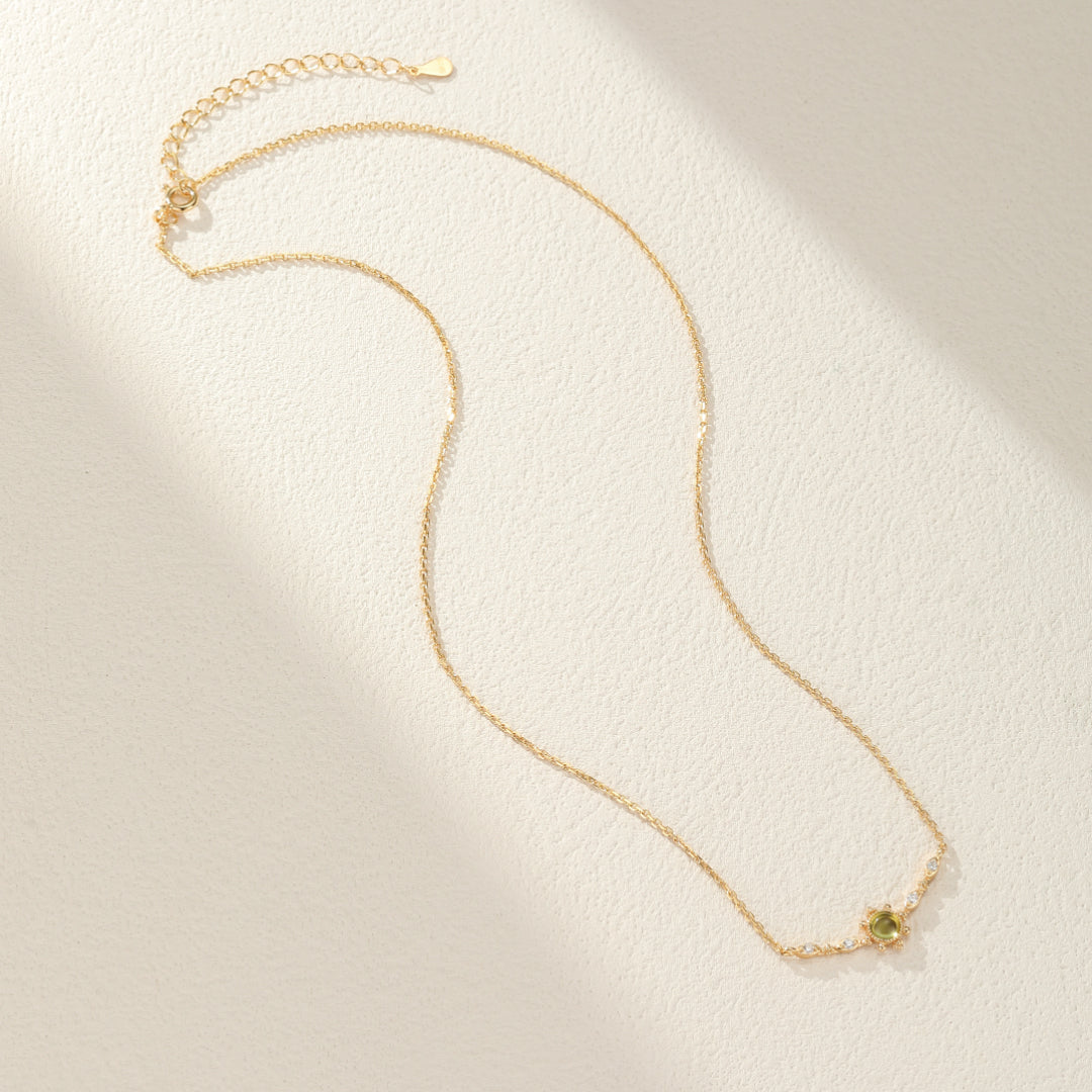 Collier fin en argent plaqué or avec une pierre centrale ronde de péridot vert entourée de petits cristaux scintillants.