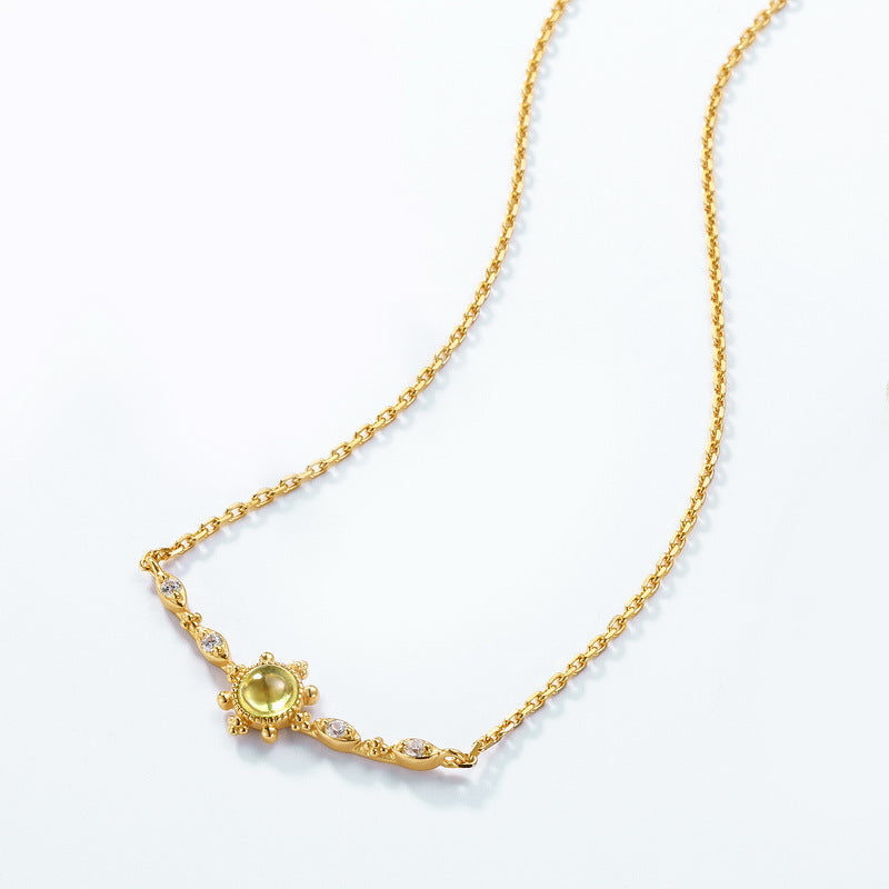 Collier en argent plaqué or avec une pierre de péridot ronde au centre, entourée de petites pierres brillantes et de détails en forme de feuille.
