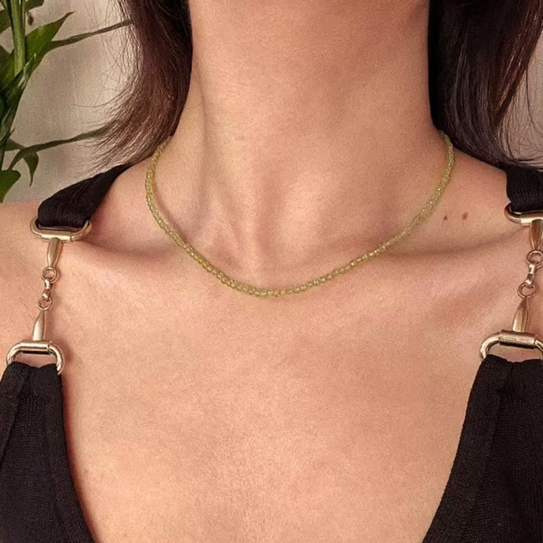 Collier ras de cou en perles fines de péridot vert pâle, présenté sur une femme portant un haut noir avec des détails métalliques dorés sur les bretelles.