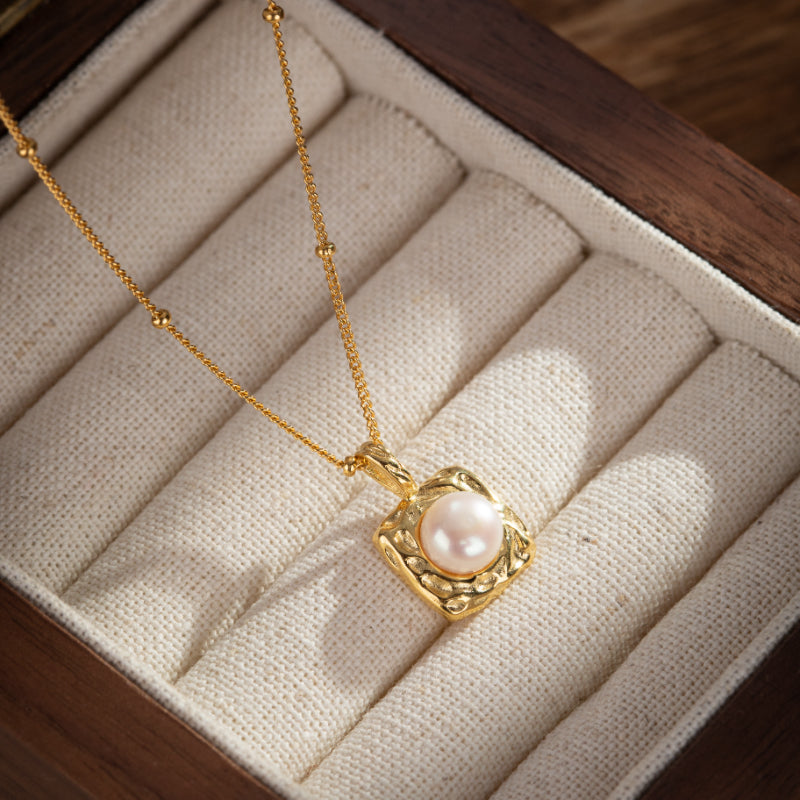 Collier en argent plaqué or avec un pendentif carré texturé serti d'une perle rose pâle délicate, présenté dans un écrin en bois.