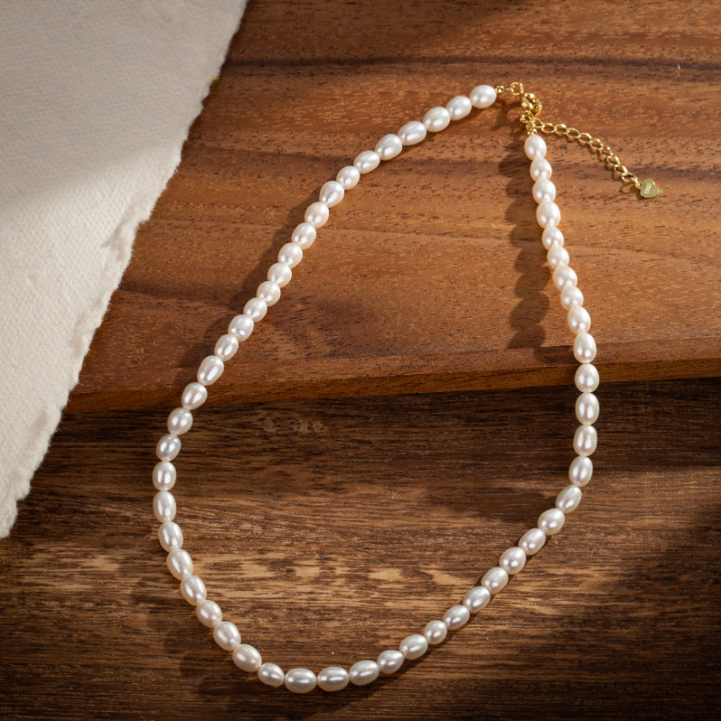 Collier ras de cou en perles d'eau douce blanches sur un fond en bois avec une texture naturelle et un tissu blanc sur le côté gauche, fermoir plaqué or.