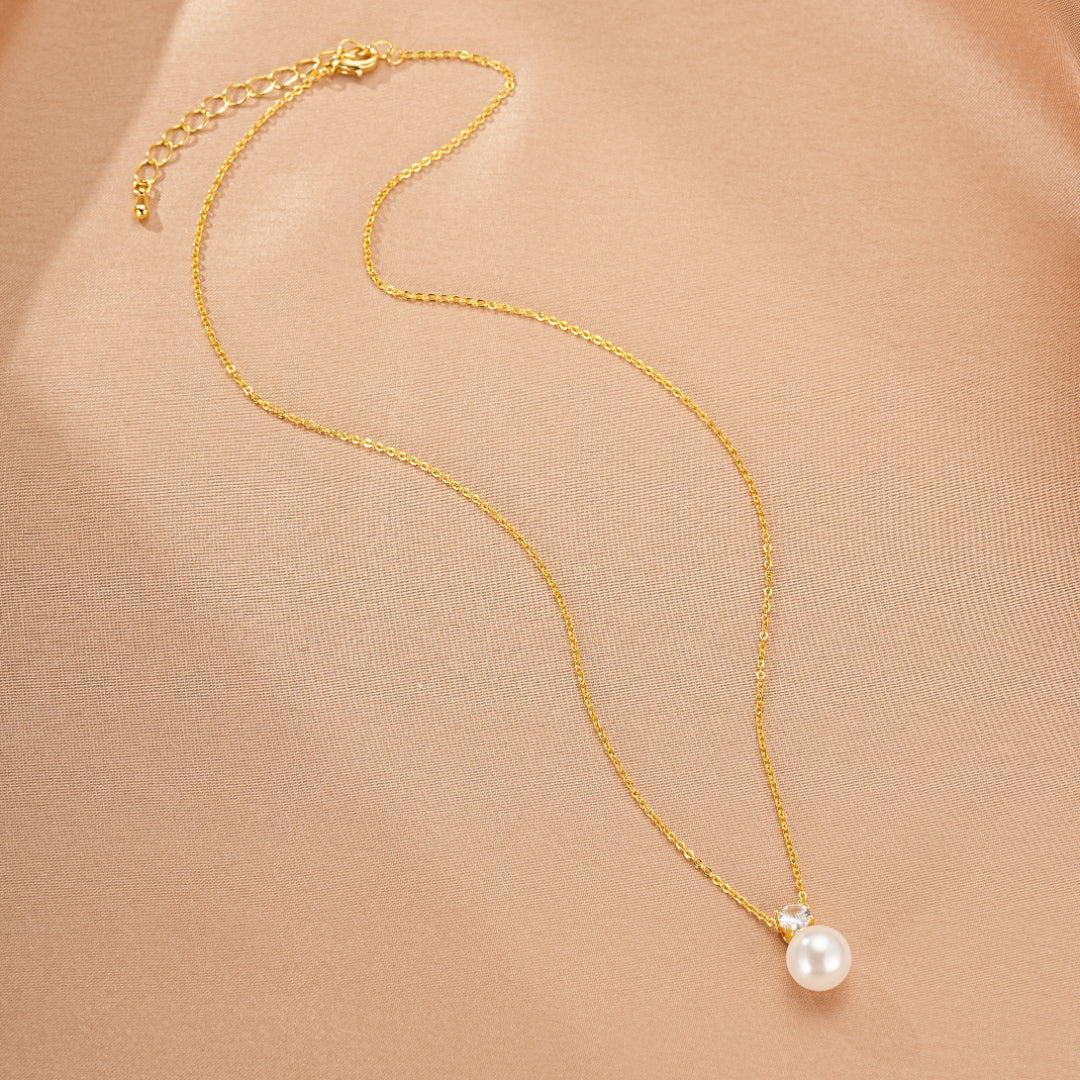 Collier fin en or avec une perle blanche et un petit zirconium cubique, sur fond beige satiné.