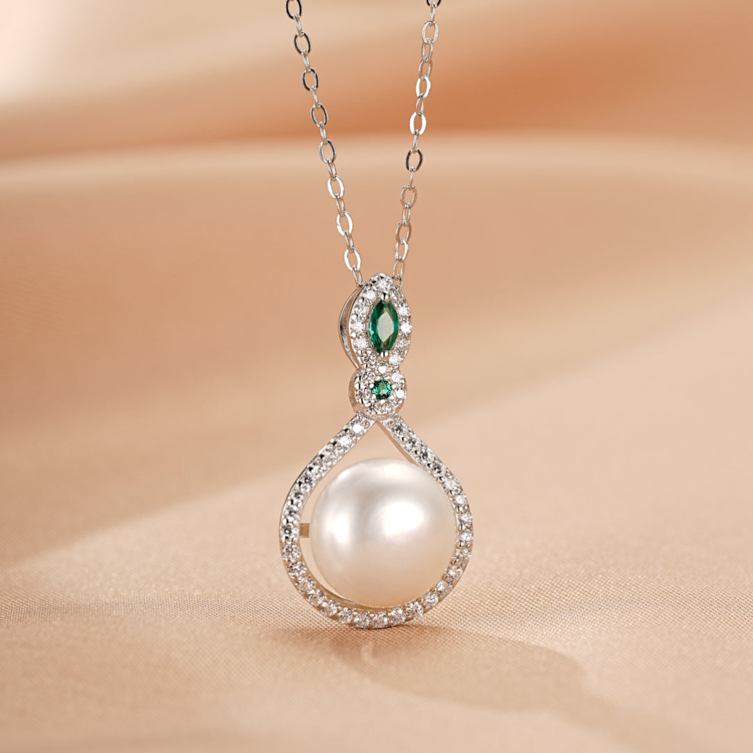Collier en argent 925 avec une perle blanche centrale, entourée de petites pierres scintillantes et ornée d'émeraudes en forme de marquise.