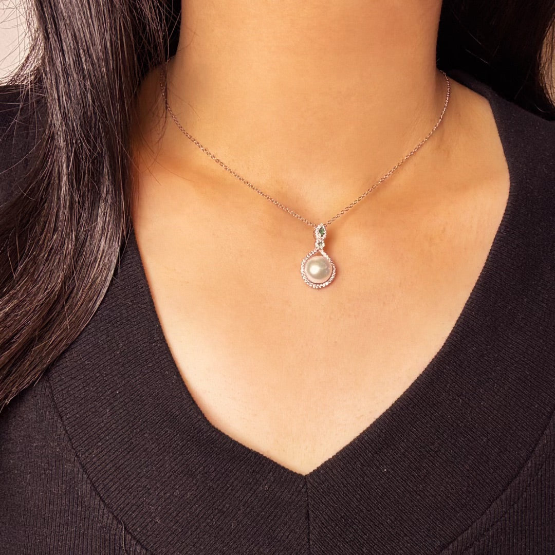 Gros plan sur un collier en argent 925 avec un pendentif rond orné d'une perle nacrée et de petites pierres scintillantes, porté par une femme.