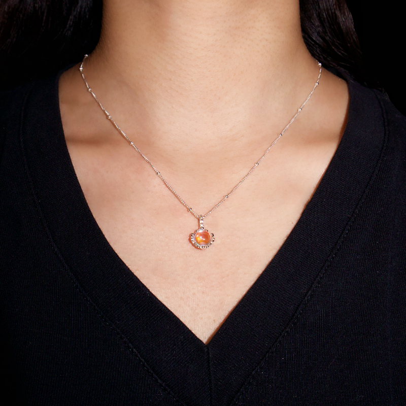 Collier ras du cou en argent 925 avec un pendentif en forme de cœur orange, orné d'une pierre de lune et de petits cristaux scintillants, porté par une femme.
